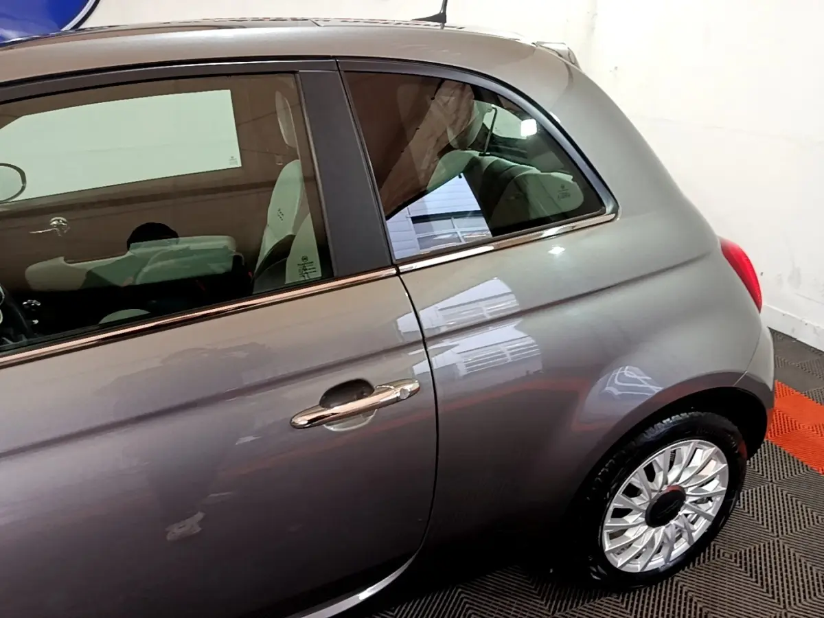 Vue côté gauche arrière d'une FIAT 500 Dolcevita hybride gris foncé avec jante argentée et poignée chromée.