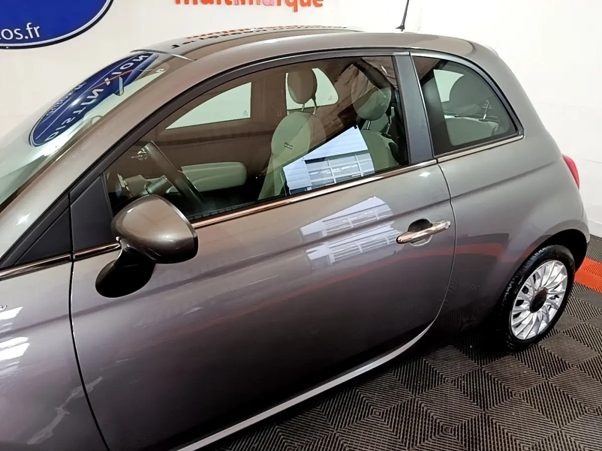 Vue latérale droite d'une Fiat 500 Dolcevita hybride gris foncé avec jantes distinctives et intérieur clair visible.