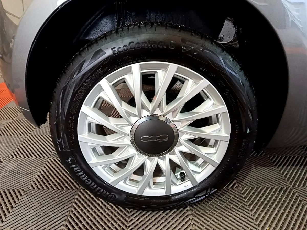 Gros plan sur la roue avant droite d'une FIAT 500 gris foncé, avec jante alliage au design étoilé.