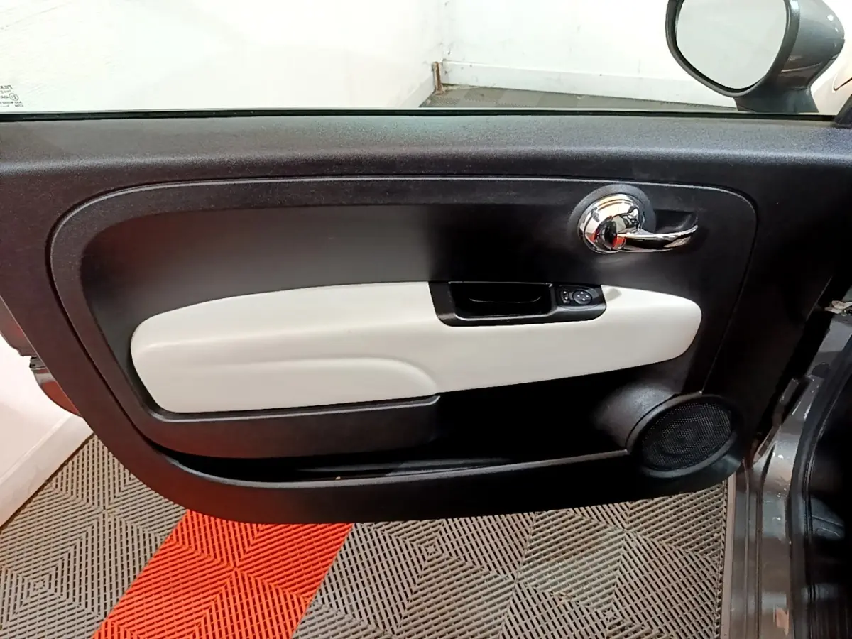 Vue intérieure du panneau de porte côté gauche de la Fiat 500 gris foncé avec poignée chrome et accoudoir clair.