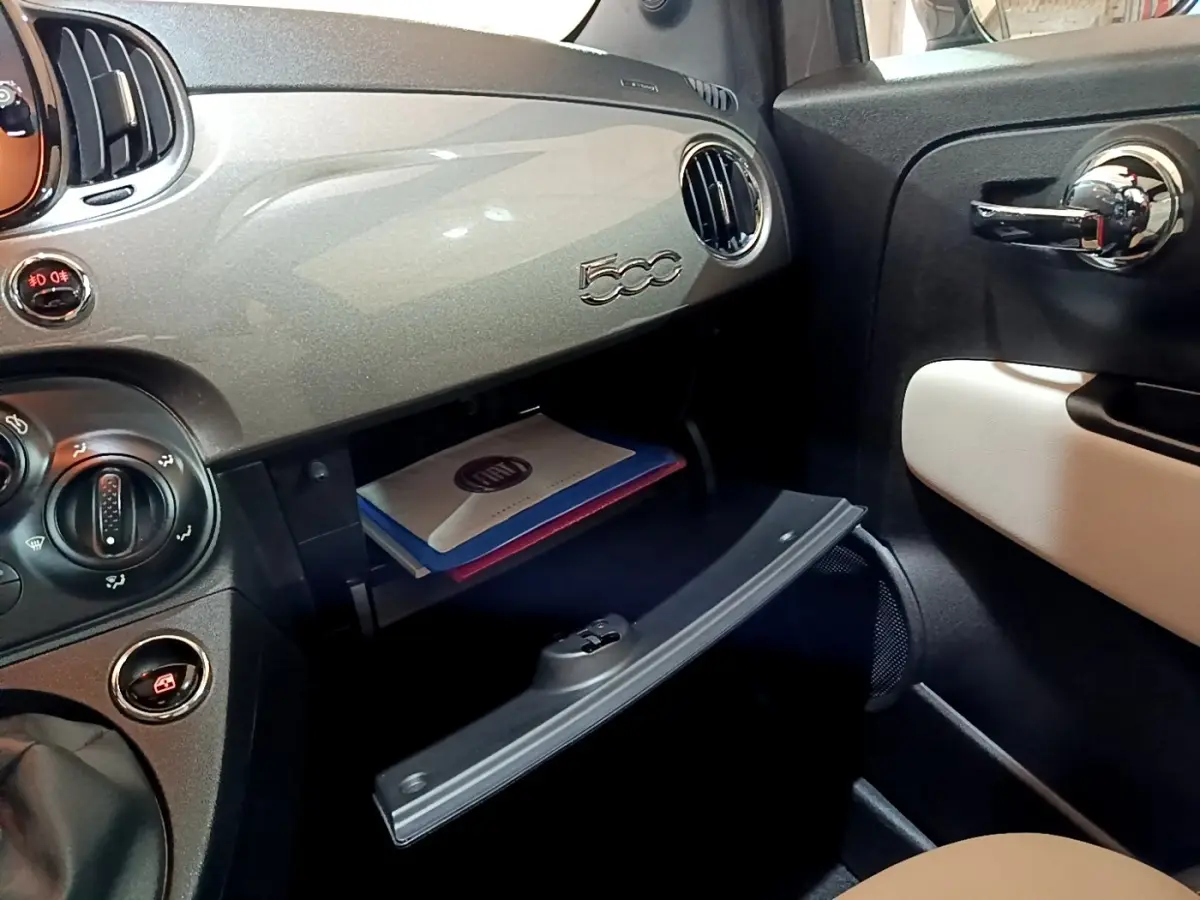 Vue intérieure côté passager du tableau de bord gris foncé de la FIAT 500 avec boîte à gants ouverte et porte chromée.