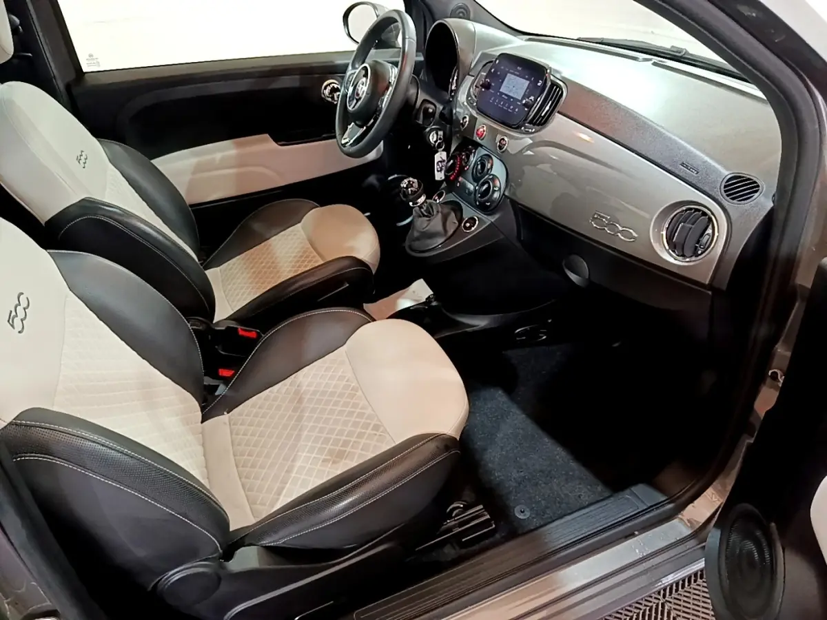 Vue intérieure côté conducteur de la Fiat 500 Hybrid 2021 avec sièges bi-ton beige et noir et tableau de bord gris.