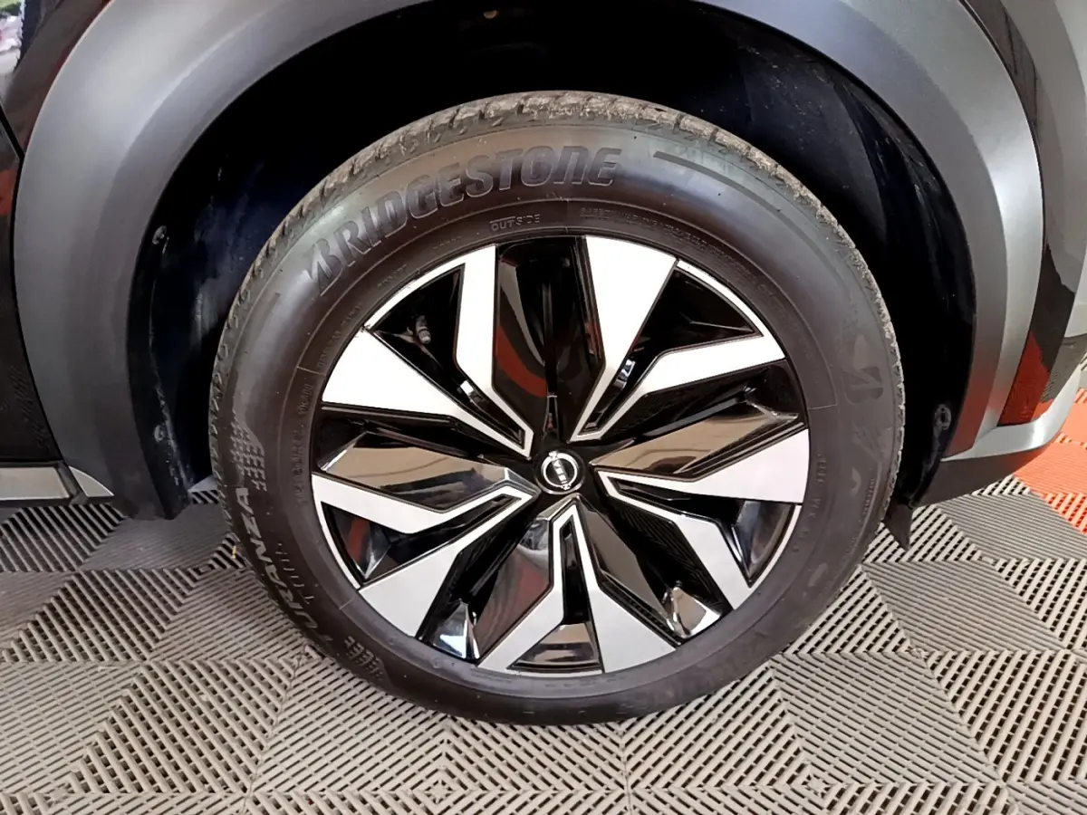 Gros plan sur la roue avant droite du Nissan Juke noir 2023, mettant en valeur la jante bicolore brillante et le pneu Bridgestone.
