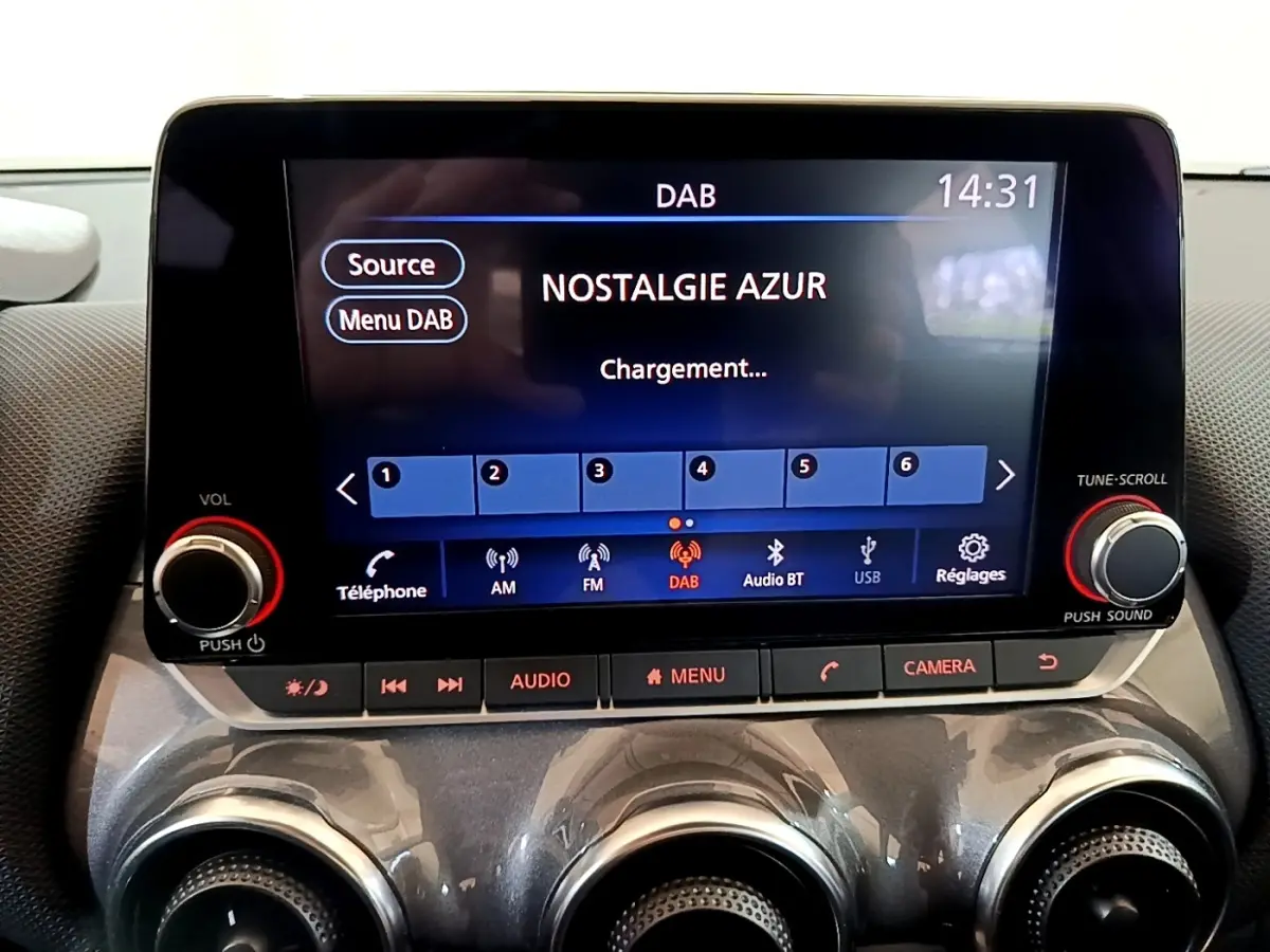 Écran tactile central du Nissan Juke noir 2023 affichant la radio DAB avec commandes audio et climatisation en dessous.