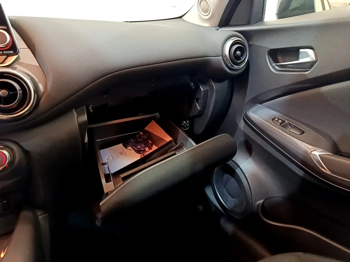 Intérieur côté passager du Nissan Juke noir 2023, avec boîte à gants ouverte et tableau de bord texturé.