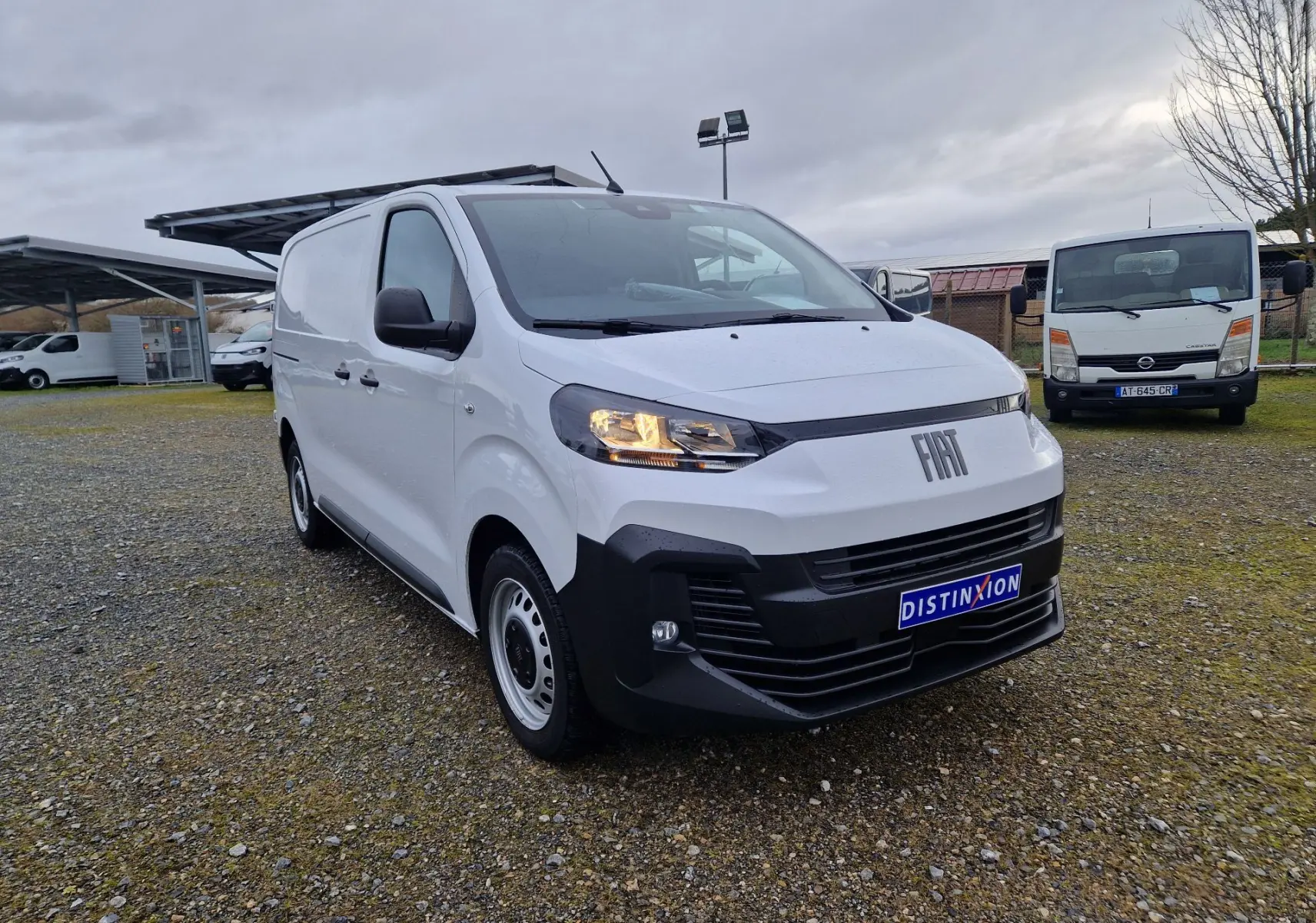 Fiat Scudo Fourgon blanc en 3/4 avant droit, avec calandre noire et plaque de protection, sur parking extérieur.