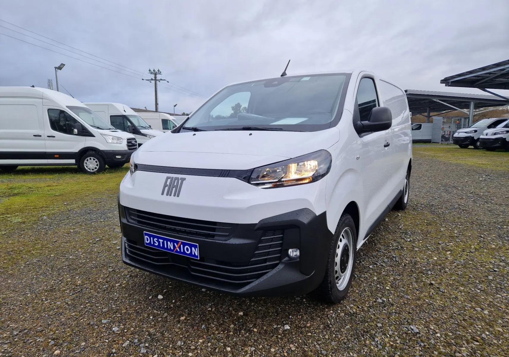 Fiat Scudo Fourgon blanc en 3/4 avant droit, avec calandre noire et phares allumés sur terrain extérieur.