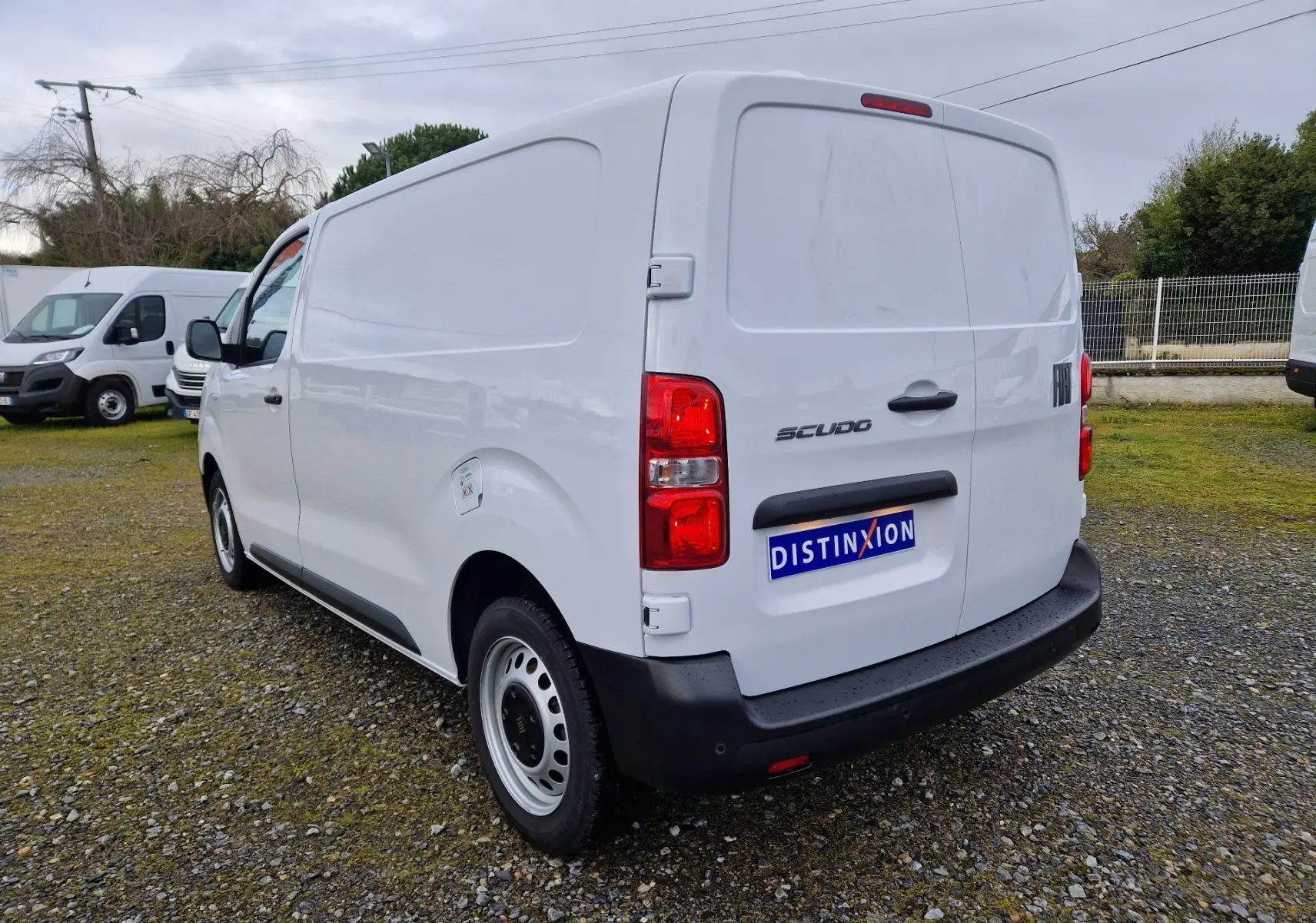 Vue 3/4 arrière droite d’un FIAT Scudo Fourgon blanc 2024 avec plaque de protection et feux rouges visibles.