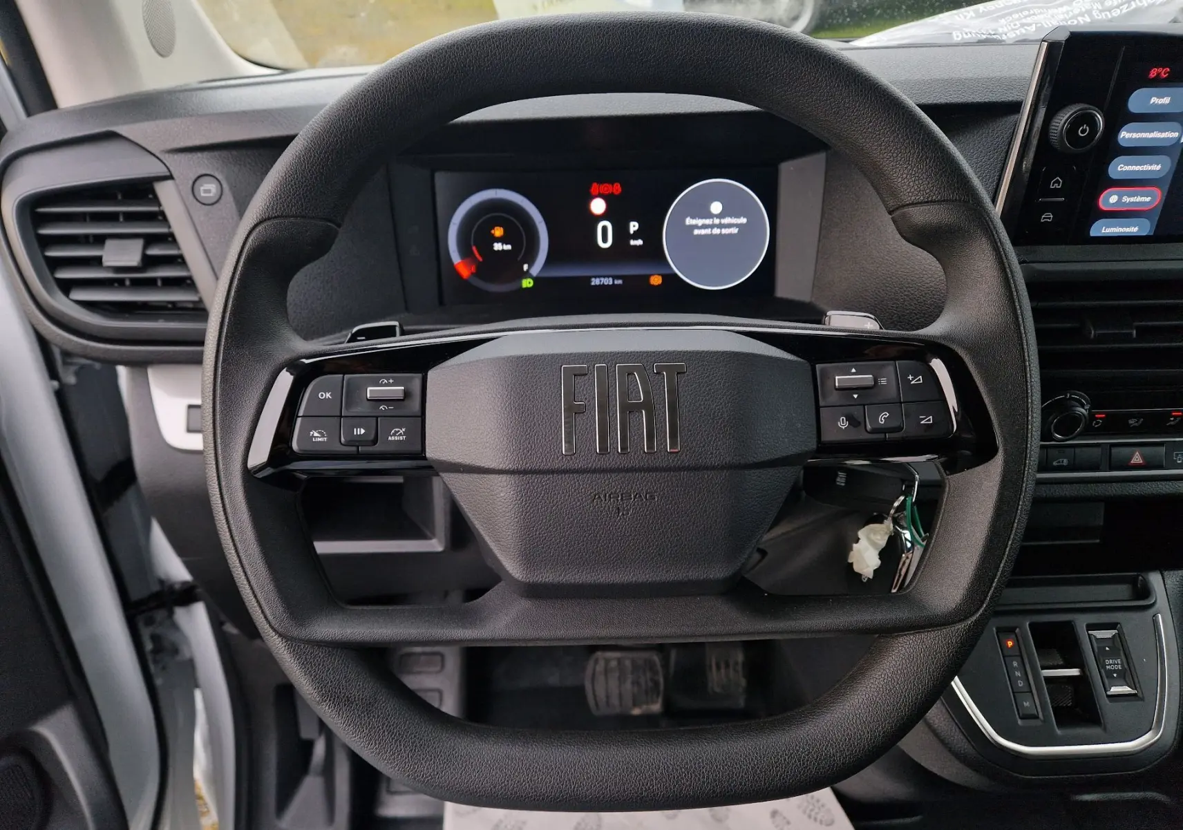 Vue intérieure centrée sur le volant noir du Fiat Scudo Fourgon 2024 avec tableau de bord numérique et console centrale visible.