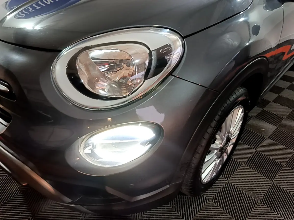 Gros plan sur l'avant droit gris foncé du FIAT 500X 2019, mettant en valeur le phare et le feu antibrouillard allumé.