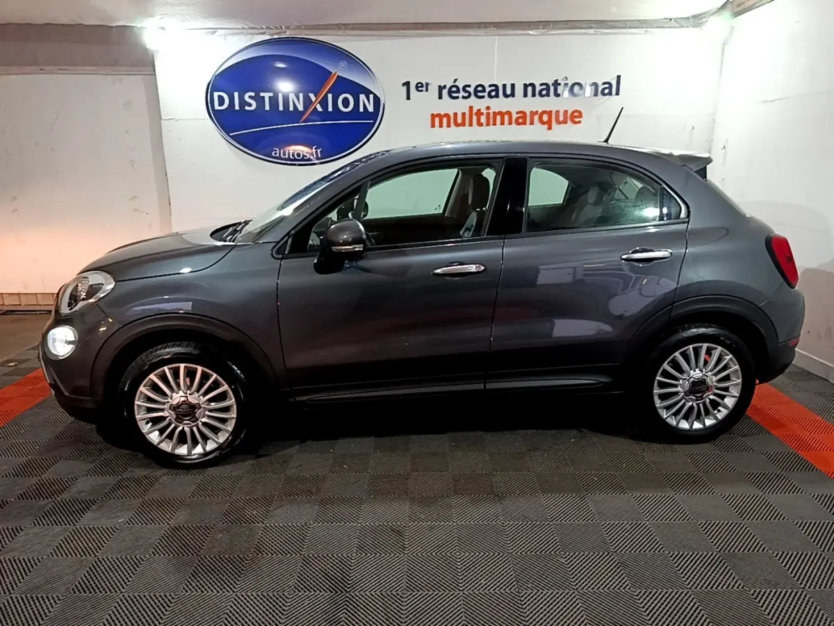 Vue de profil côté gauche d'une FIAT 500X gris foncé 2019 avec jantes alliage et rétroviseurs électriques dans un showroom.