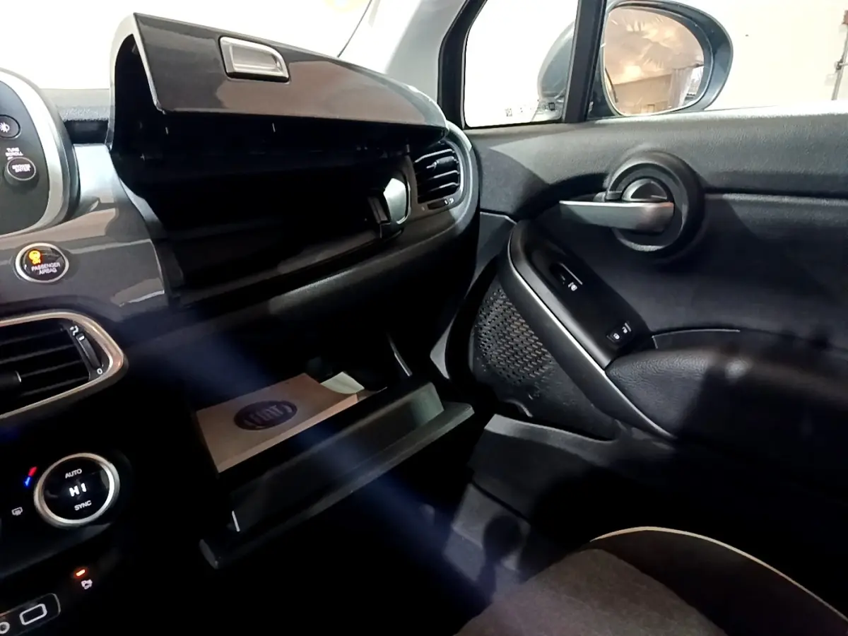 Intérieur côté passager du Fiat 500X gris foncé, avec boîte à gants ouverte et commandes de porte visibles.
