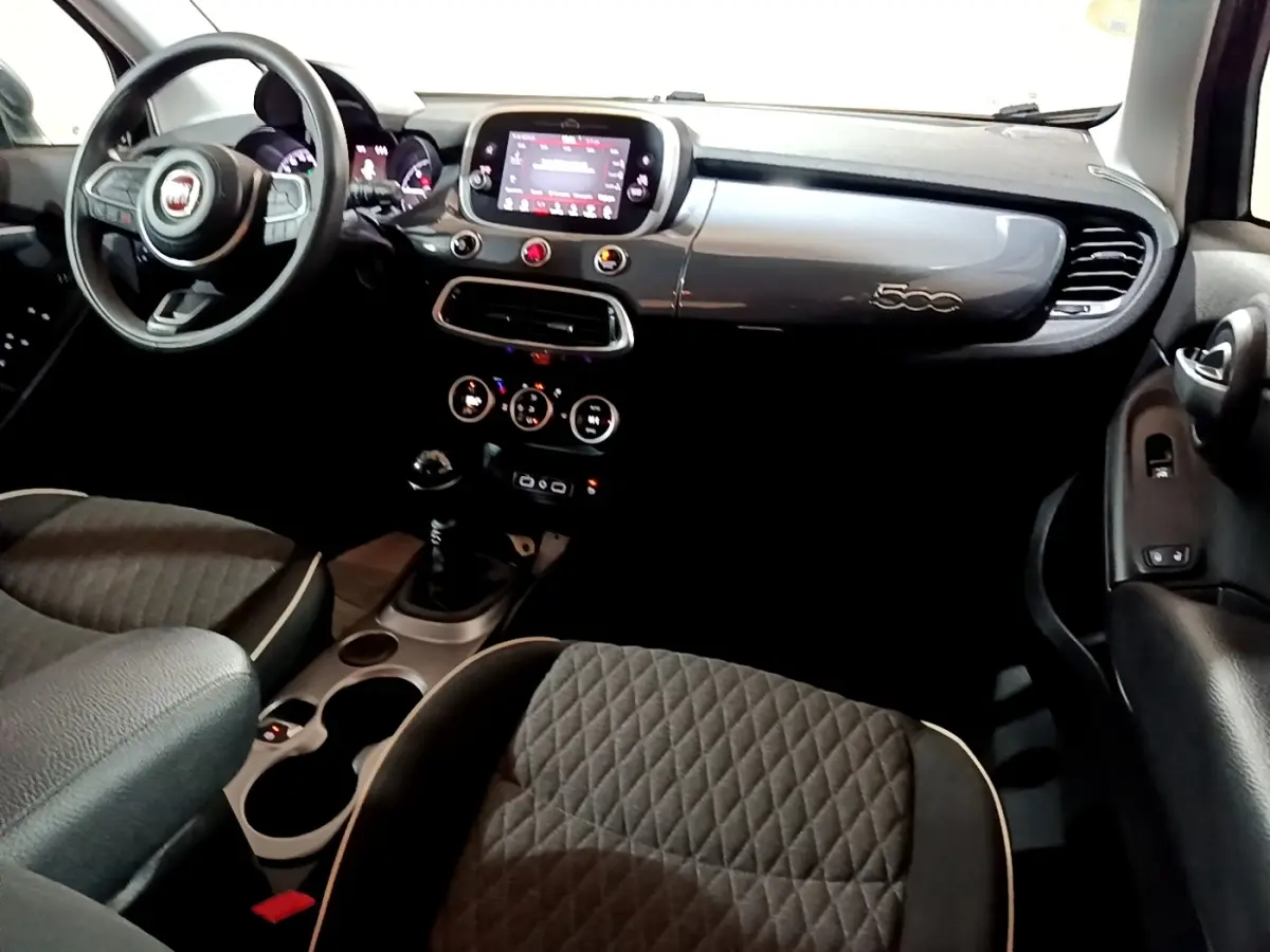 Vue intérieure avant du tableau de bord gris foncé et des sièges tissu matelassé de la Fiat 500X 1.6 Multijet 2019.
