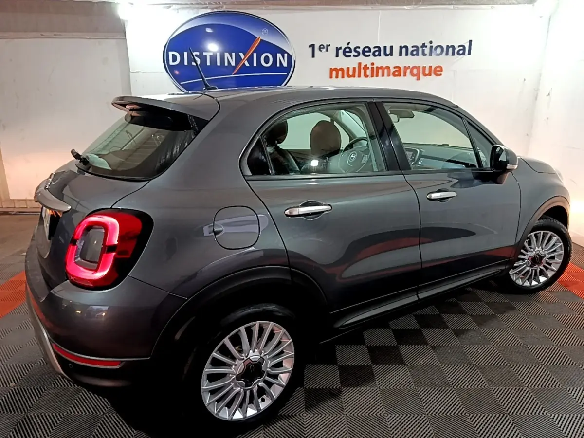 Vue 3/4 arrière droite d'une FIAT 500X gris foncé avec feux arrière allumés dans un showroom intérieur.