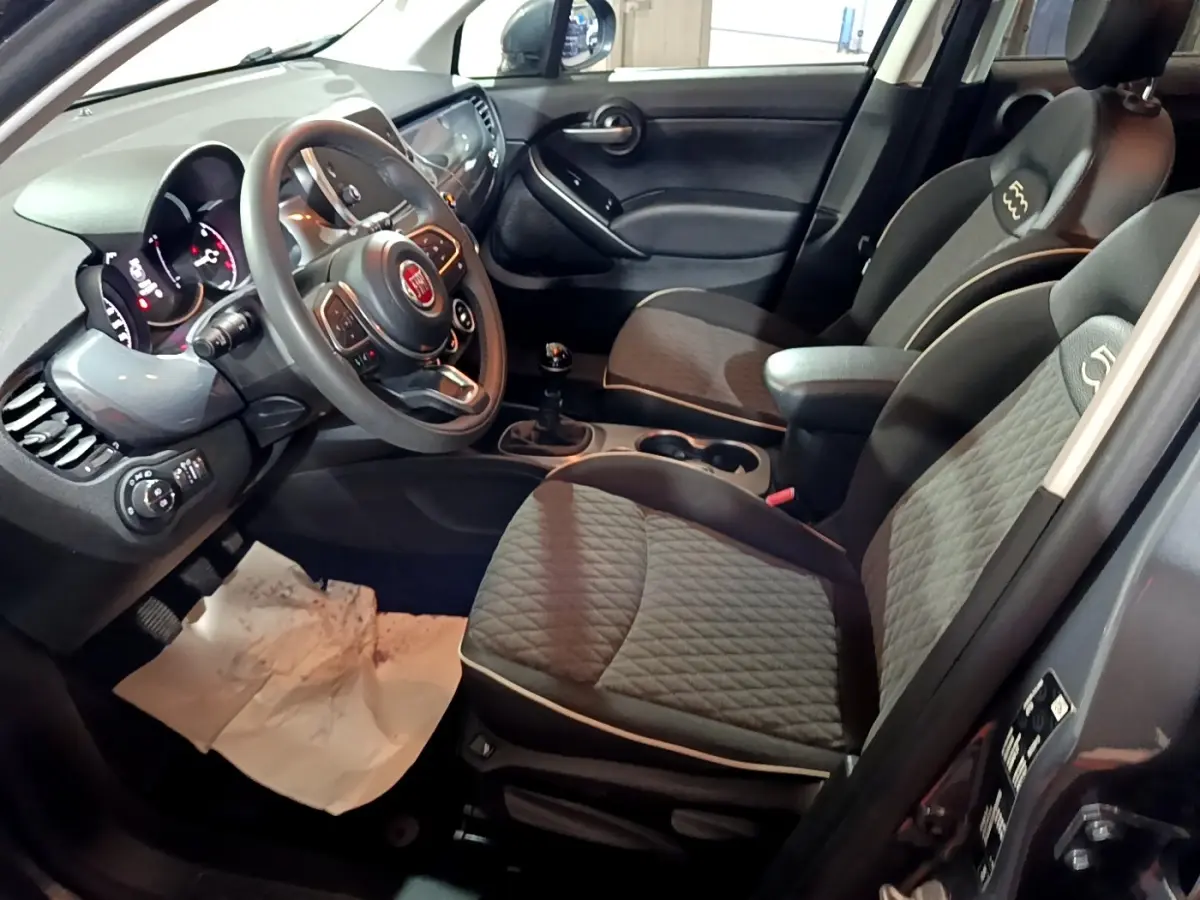 Intérieur avant droit de la FIAT 500X gris foncé, montrant sièges tissu, volant multifonctions et levier de vitesse manuel.