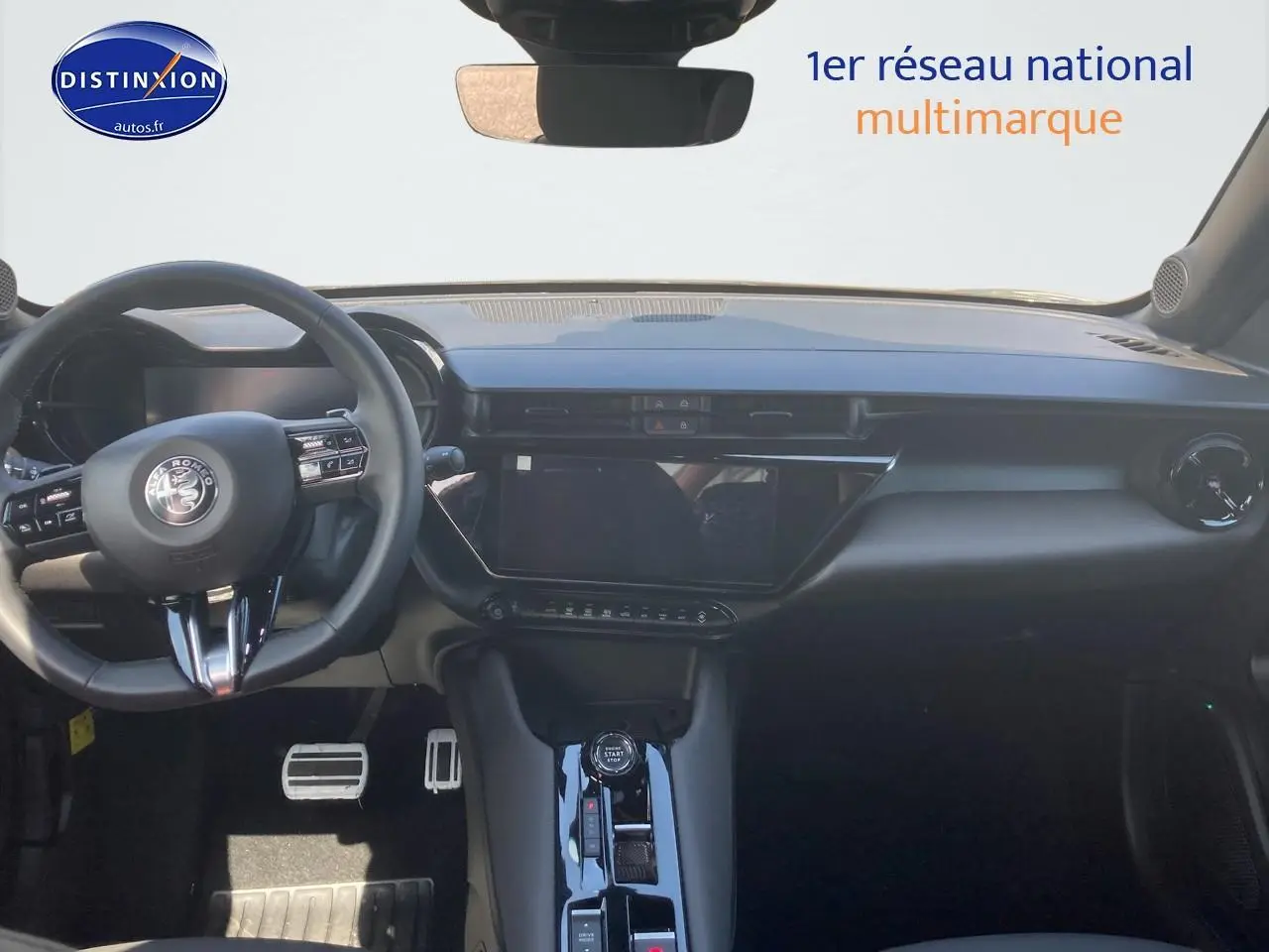Vue intérieure frontale de l'Alfa Romeo Junior 1.2 hybride 2026 avec tableau de bord noir et écran tactile central.
