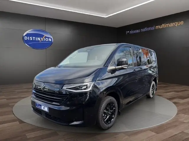 Vue 3/4 avant droit d'un Volkswagen Transporter noir 2026 avec jantes noires et phares LED dans un showroom.