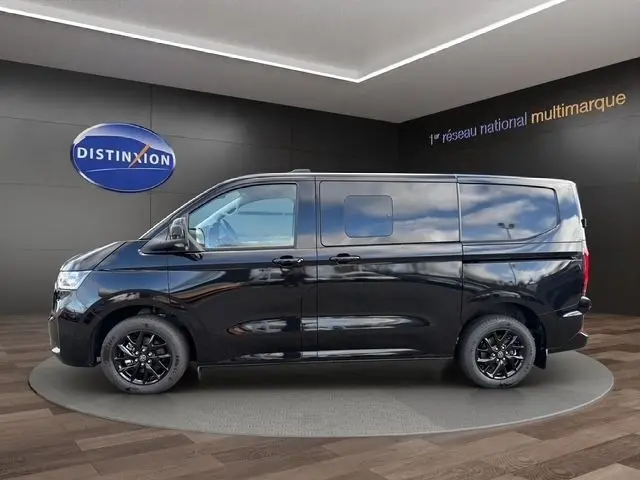 Profil latéral droit d’un Volkswagen Transporter noir, avec jantes noires et vitres teintées, sur fond intérieur showroom.