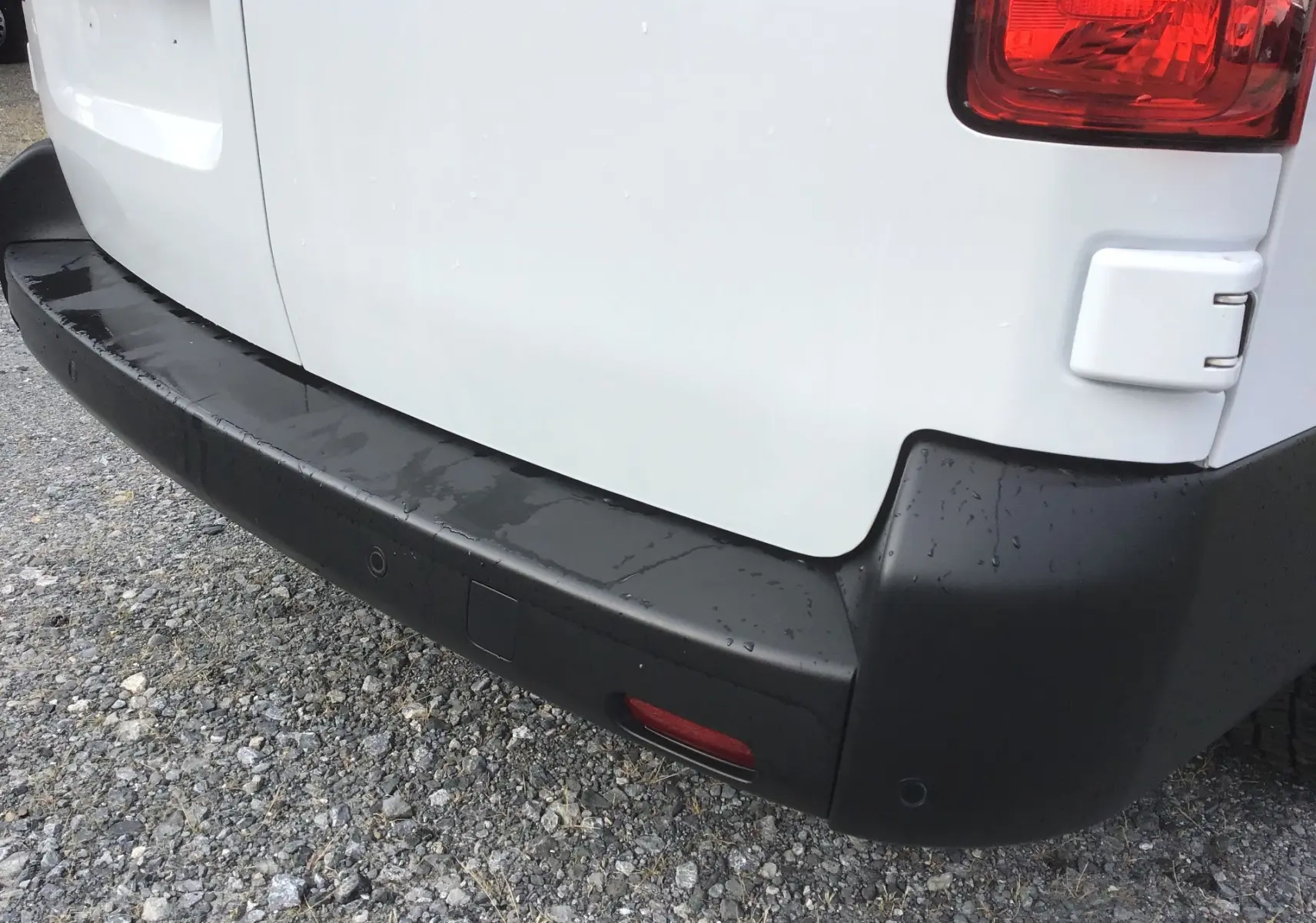 Gros plan sur le pare-chocs arrière noir du FIAT Scudo Fourgon blanc, avec feu arrière et capteurs de recul visibles.