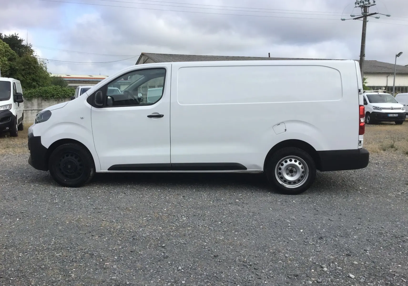 Vue de profil côté gauche d'un fourgon FIAT Scudo XL blanc 2024 avec garde au sol réhaussée et protections noires.