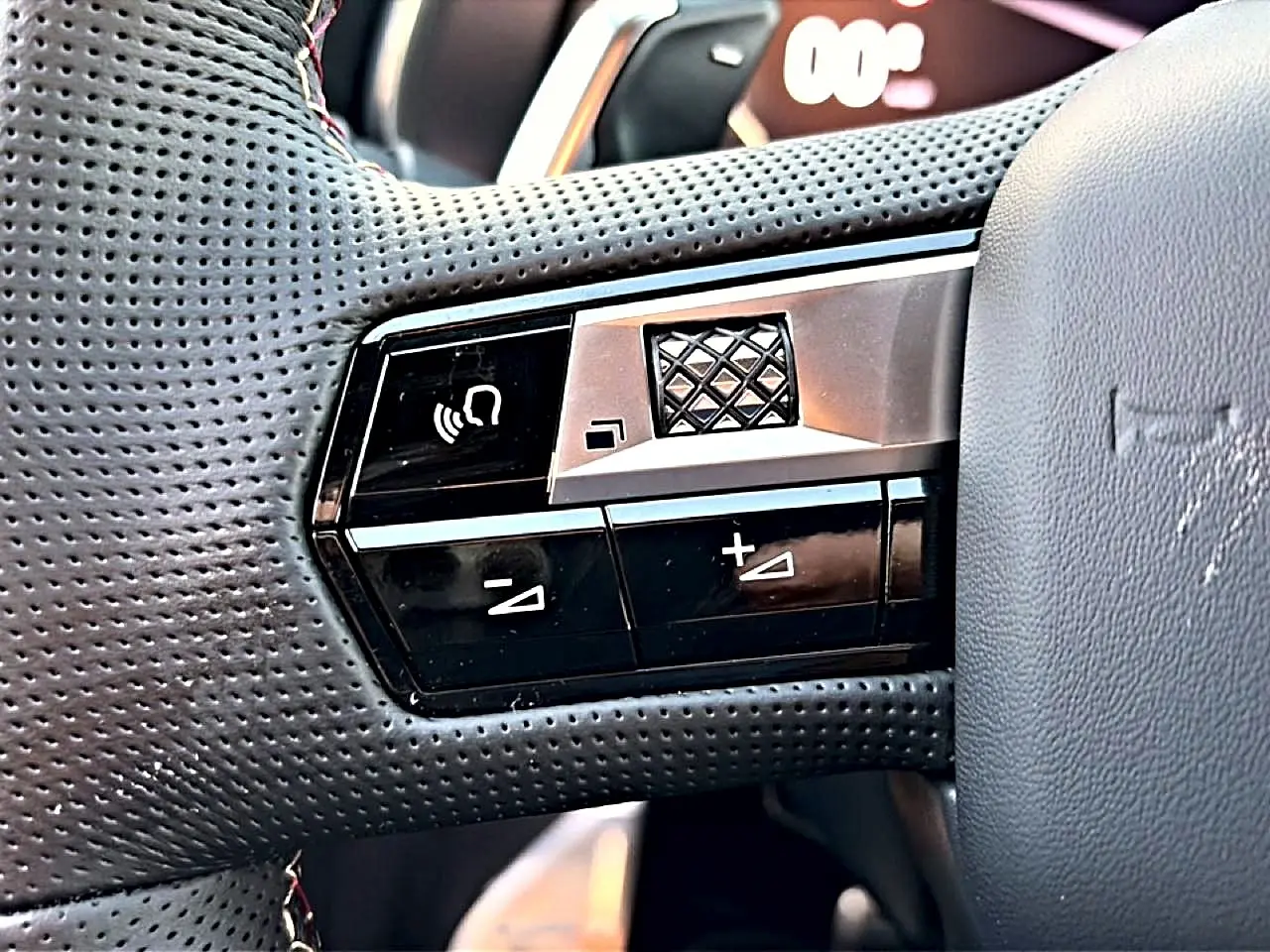 Gros plan sur les commandes gauche du volant cuir perforé du DS7 noir, avec boutons de volume et molette tactile.