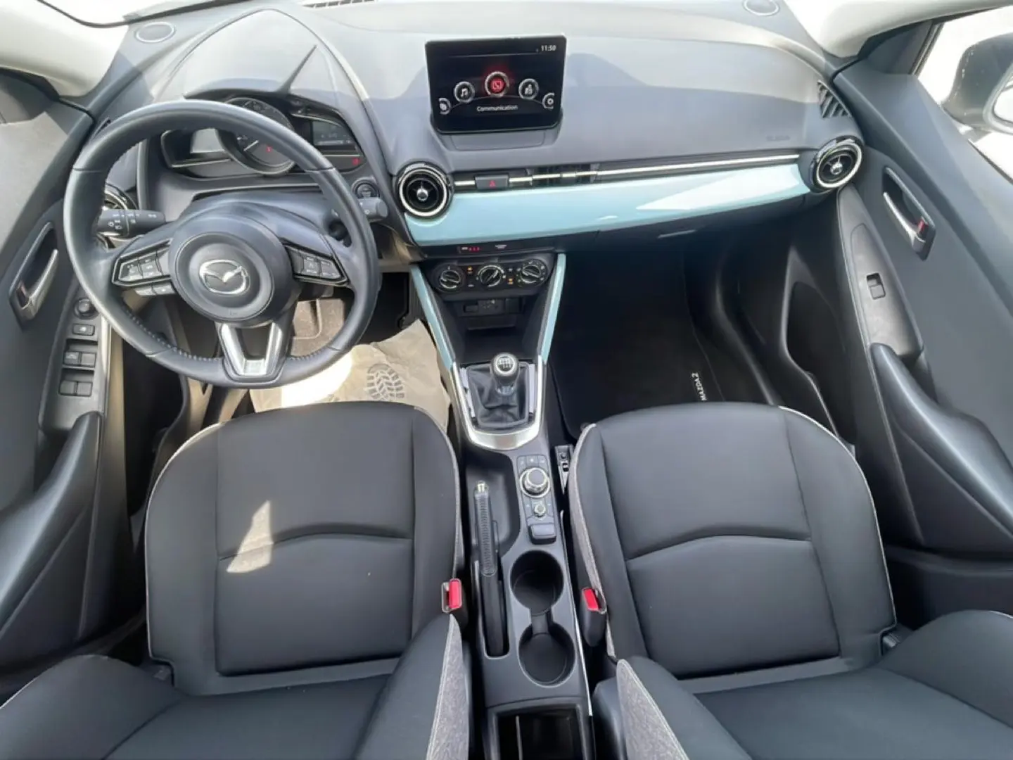 Vue intérieure avant de la Mazda2 2024, montrant tableau de bord, volant cuir multifonction et levier de vitesses manuel.