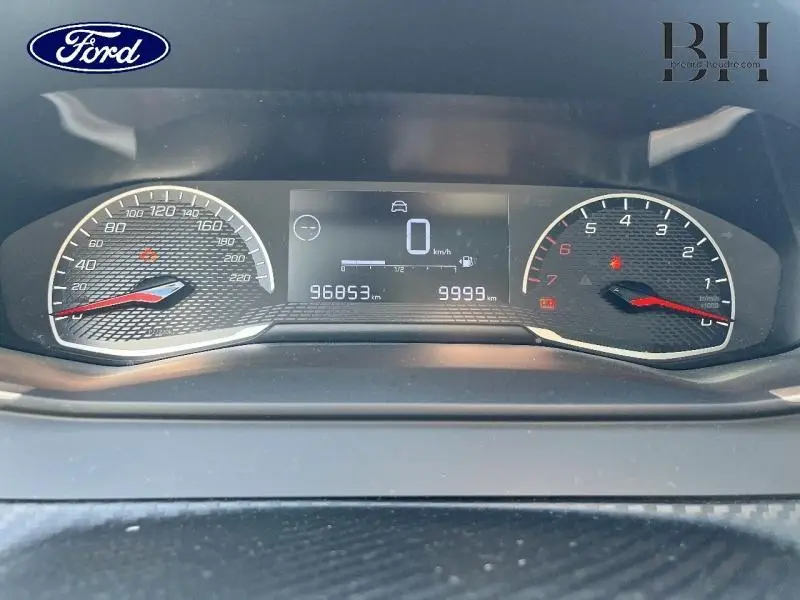 Tableau de bord numérique d'une Peugeot 208 Affaire blanc banquise, affichant vitesse à 0 km/h et compteurs éclairés.