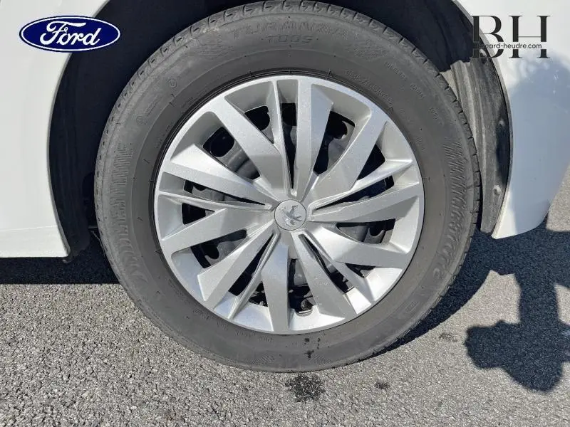 Gros plan sur la roue avant droite d'une Peugeot 208 Affaire blanche avec enjoliveur argenté au design moderne.