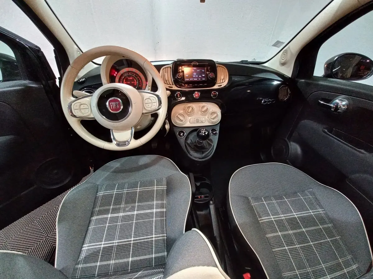 Vue intérieure avant de la Fiat 500 noire, volant beige, tableau de bord noir brillant avec écran tactile central.