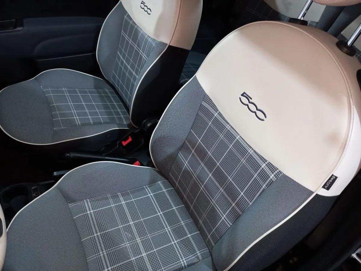 Gros plan sur les sièges avant gris à motif carreaux avec appuie-têtes blancs et logo 500 brodé dans l’habitacle d’une Fiat 500.