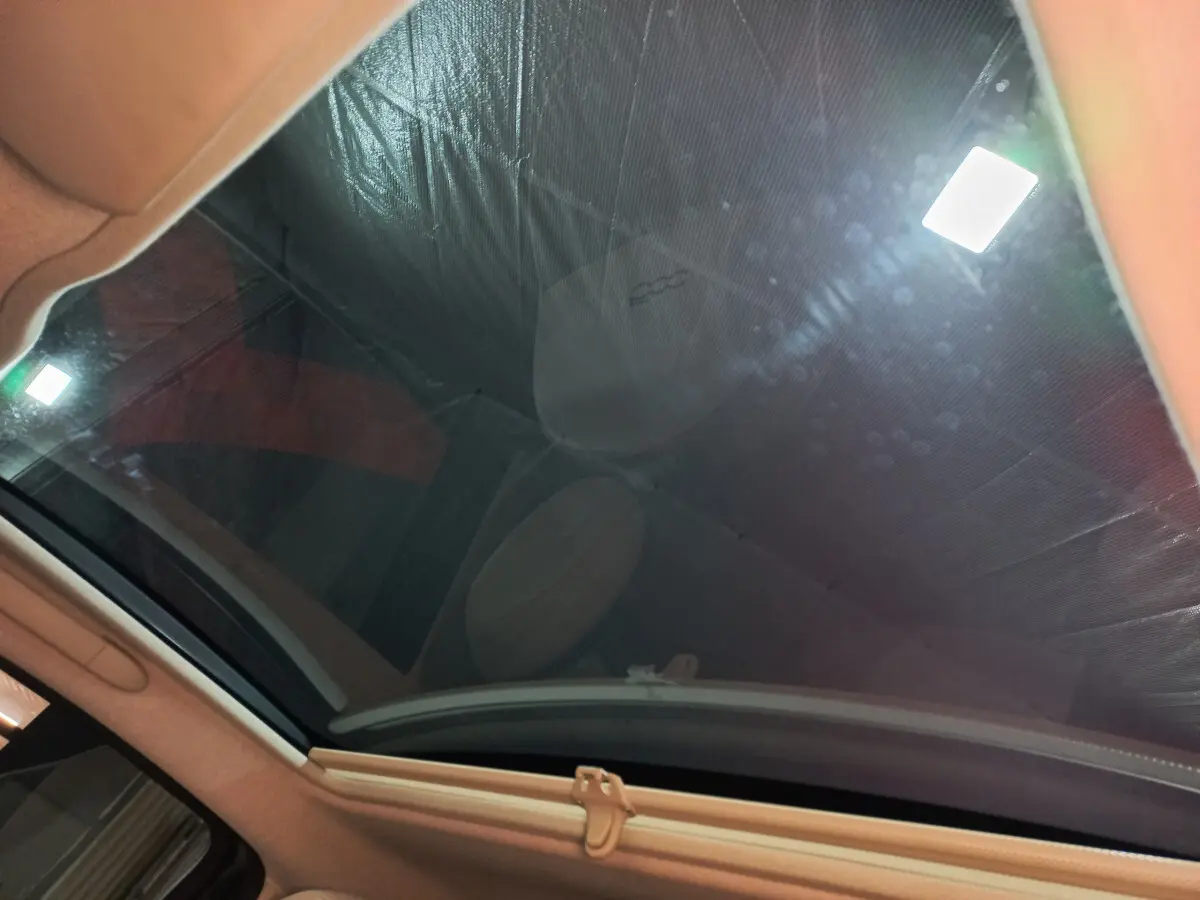 Toit panoramique en verre de la FIAT 500 noire, vue intérieure vers le ciel avec reflet du siège avant.