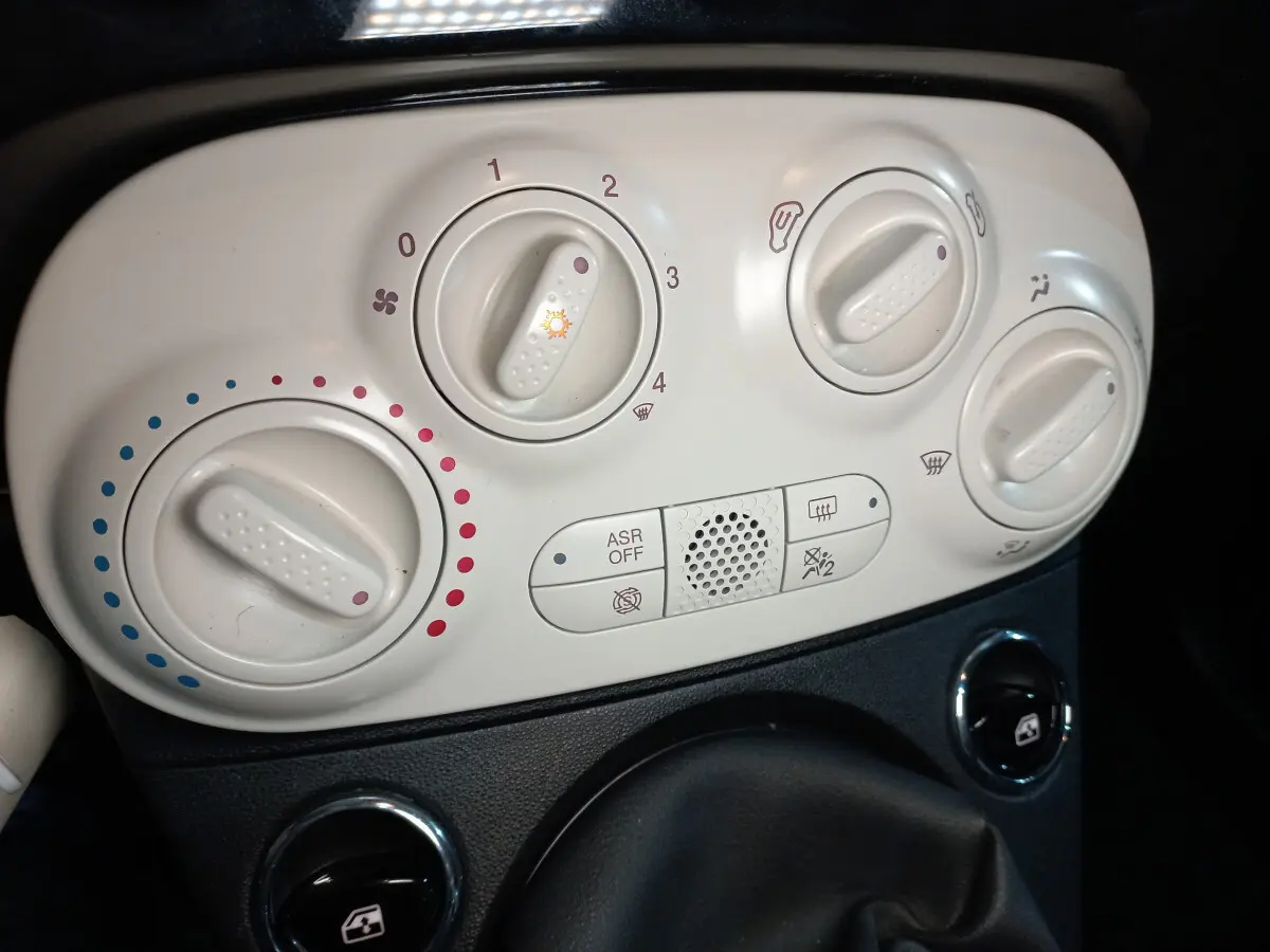 Gros plan sur les commandes de climatisation blanches du tableau de bord de la Fiat 500 noire, version Lounge 2018.