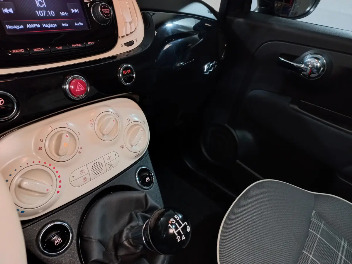 Vue rapprochée de l’intérieur côté passager d’une Fiat 500 noire, montrant la console centrale et le levier de vitesses manuel.
