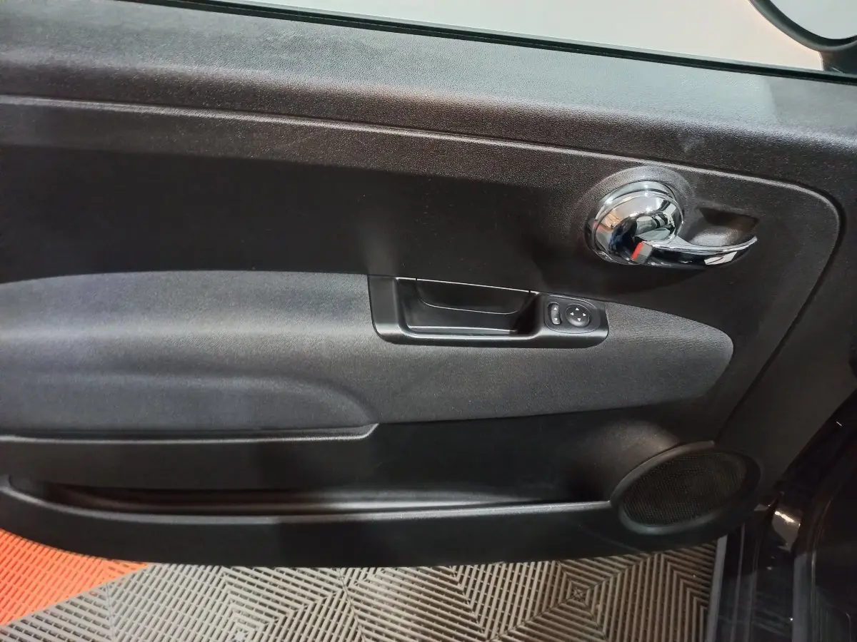 Vue rapprochée de la porte intérieure côté conducteur noire de la FIAT 500 Lounge avec poignée chromée et commandes électriques.