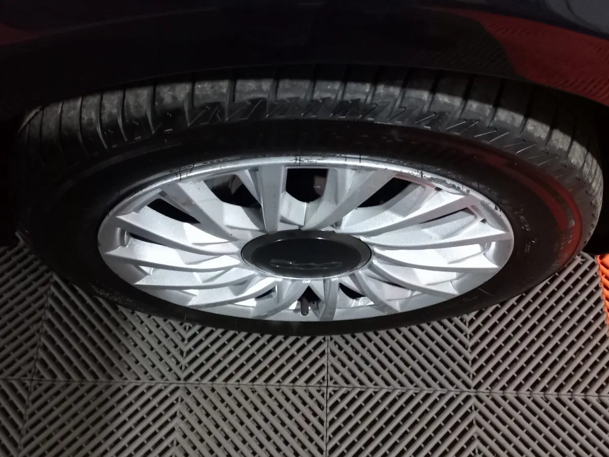 Gros plan sur la roue avant droite d'une FIAT 500 noire, mettant en valeur la jante argentée au design étoilé.