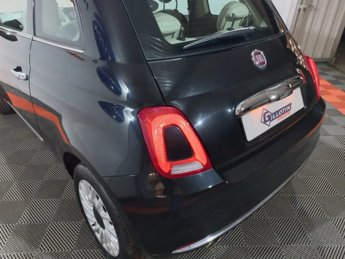 Vue 3/4 arrière droite d'une FIAT 500 noire 2018 avec feux arrière allumés et jantes argentées sur sol damier.