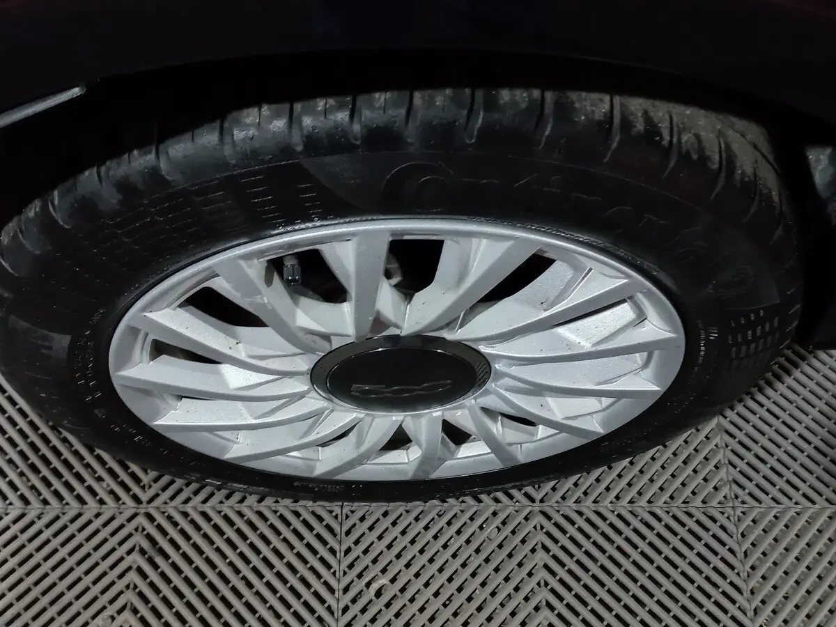 Gros plan sur la roue avant droite d’une FIAT 500 noire, mettant en valeur la jante argentée au design en étoile.