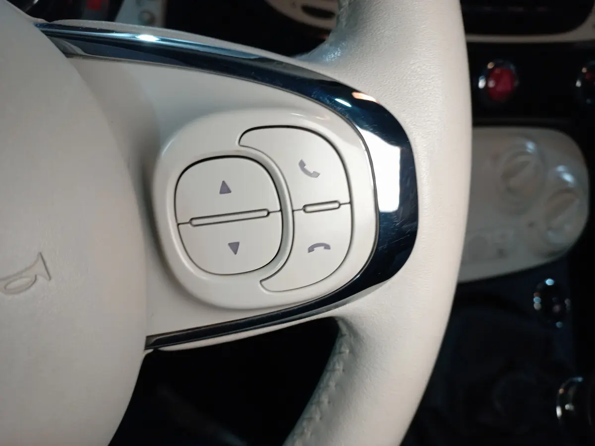 Gros plan sur les commandes blanches du volant cuir côté gauche de la Fiat 500 Lounge noire de 2018.