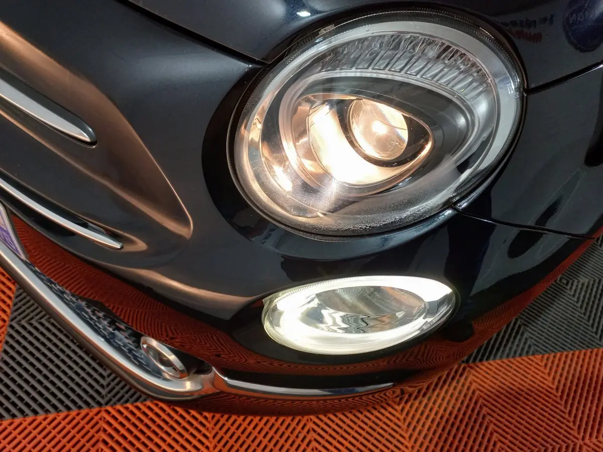 Gros plan sur l'avant droit noir d'une Fiat 500 2018, mettant en valeur ses phares allumés et antibrouillards.