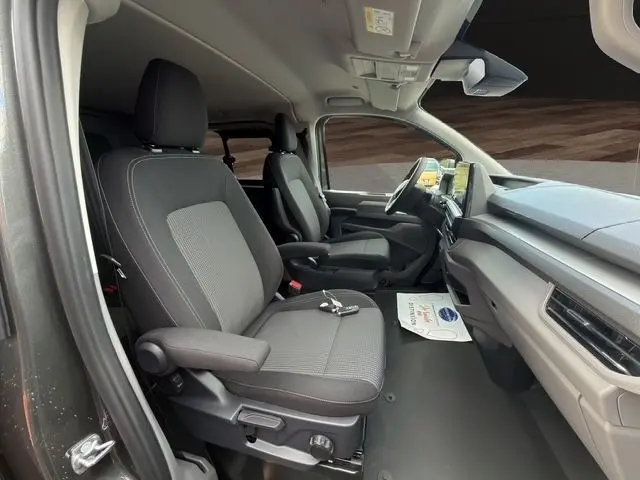 Vue intérieure côté conducteur du Volkswagen Transporter gris foncé 2026, avec sièges tissu et tableau de bord moderne.
