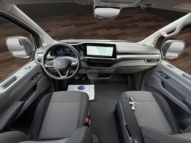Vue intérieure avant du Volkswagen Transporter gris foncé 2026, tableau de bord moderne avec écran tactile central et volant multifonctions.