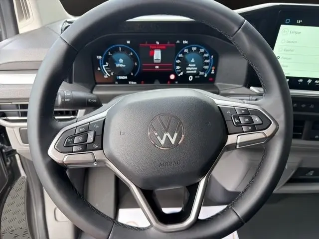 Vue rapprochée du volant multifonctions noir du Volkswagen Transporter 2026 avec tableau de bord digital et écran tactile.