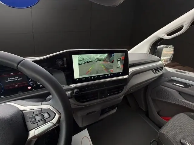 Vue intérieure côté conducteur du Volkswagen Transporter gris foncé, mettant en valeur l'écran tactile central et le volant multifonctions.
