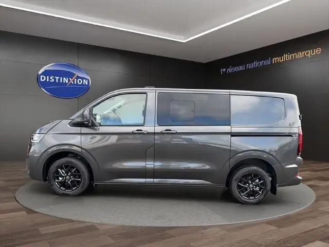 Vue latérale droite d'un Volkswagen Transporter gris foncé avec jantes noires, présenté en intérieur showroom.