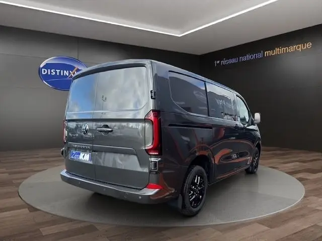 Vue 3/4 arrière droite d'un Volkswagen Transporter gris foncé avec vitres teintées et jantes noires en showroom.