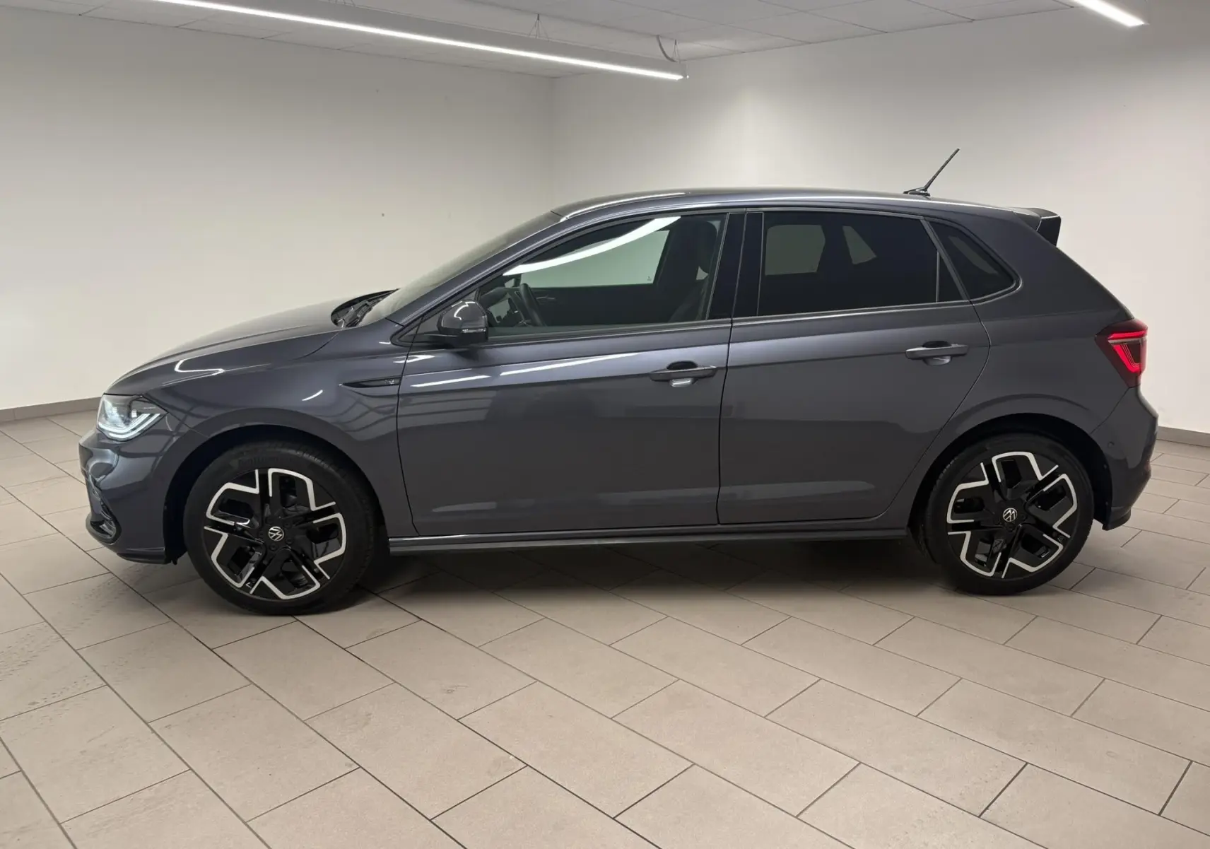 Volkswagen Polo 1.0 TSI R-Line gris cendré vue de profil côté gauche avec jantes alliage distinctives en intérieur blanc.