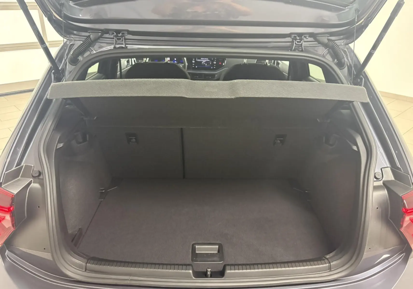 Coffre ouvert vu de l'arrière d'une Volkswagen Polo gris cendré, avec plage arrière relevée et intérieur spacieux.