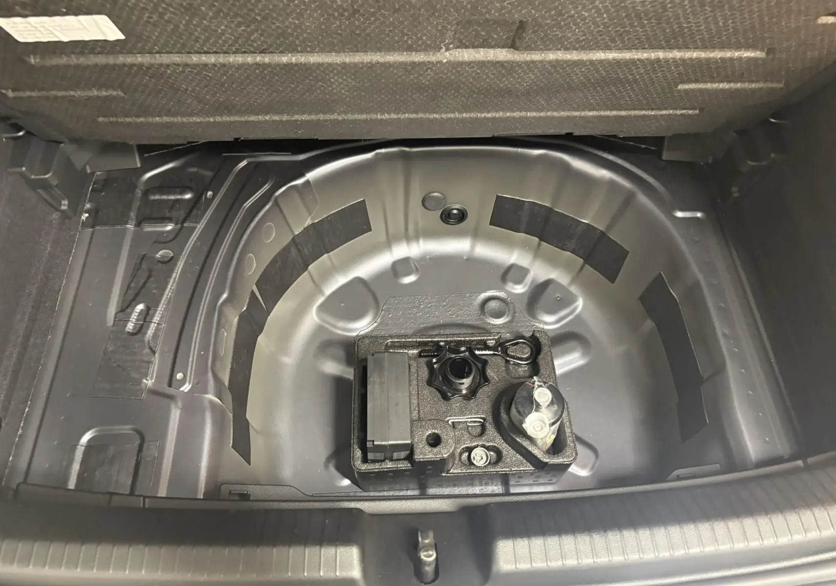 Coffre ouvert d'une Volkswagen Polo gris cendré, vue plongeante sur le rangement sous plancher sans roue de secours.