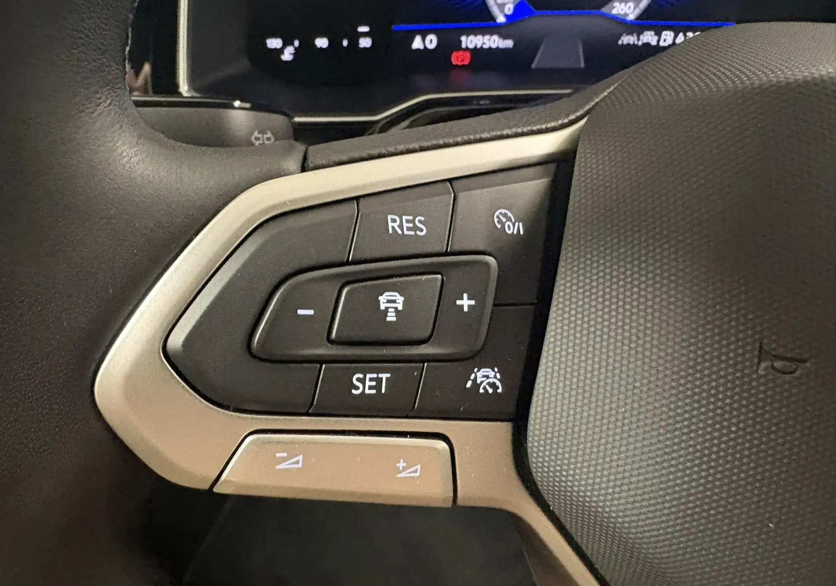 Gros plan sur les commandes de régulateur de vitesse au volant d'une Volkswagen Polo gris cendré, tableau de bord numérique en arrière-plan.