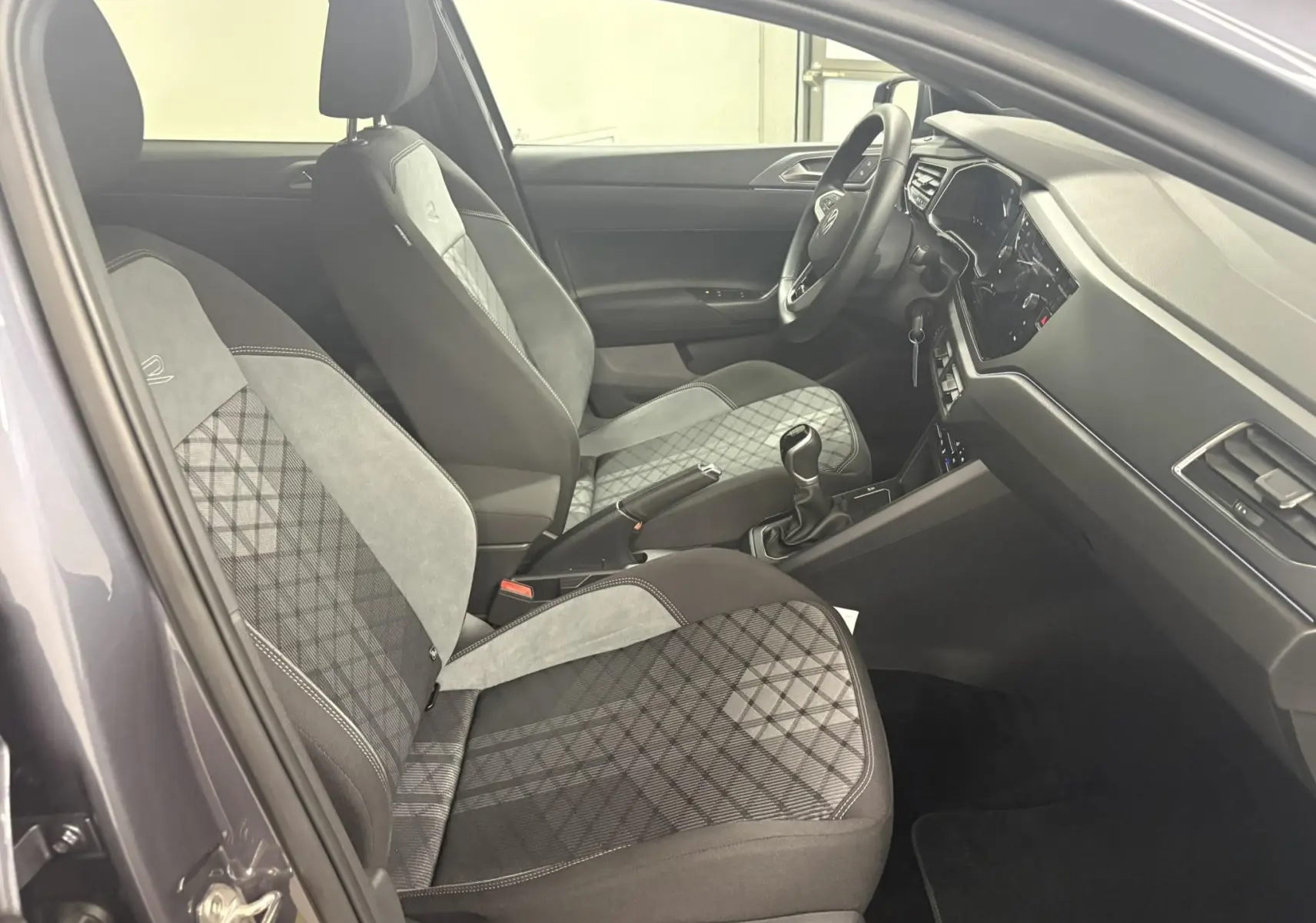 Vue intérieure côté conducteur de la Volkswagen Polo 1.0 TSI R-Line 2025 avec sièges tissu gris à motif et volant multifonction.